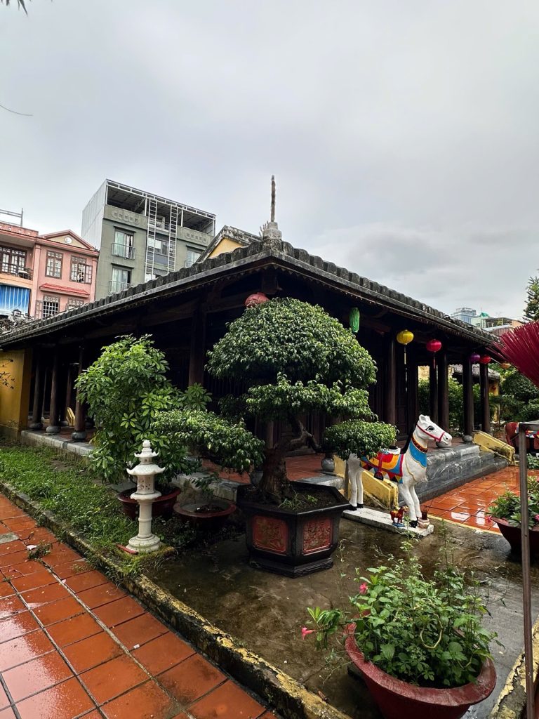 The old wooden communal house of Hải Châu village in Da Nang, with a bonsai tree, a painted horse statue and lanterns under its tiled roof