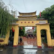 The yellow triple gate of Đình Làng Hải Châu in Da Nang, with Chinese characters, red lanterns and the communal house behind a wet tiled courtyard
