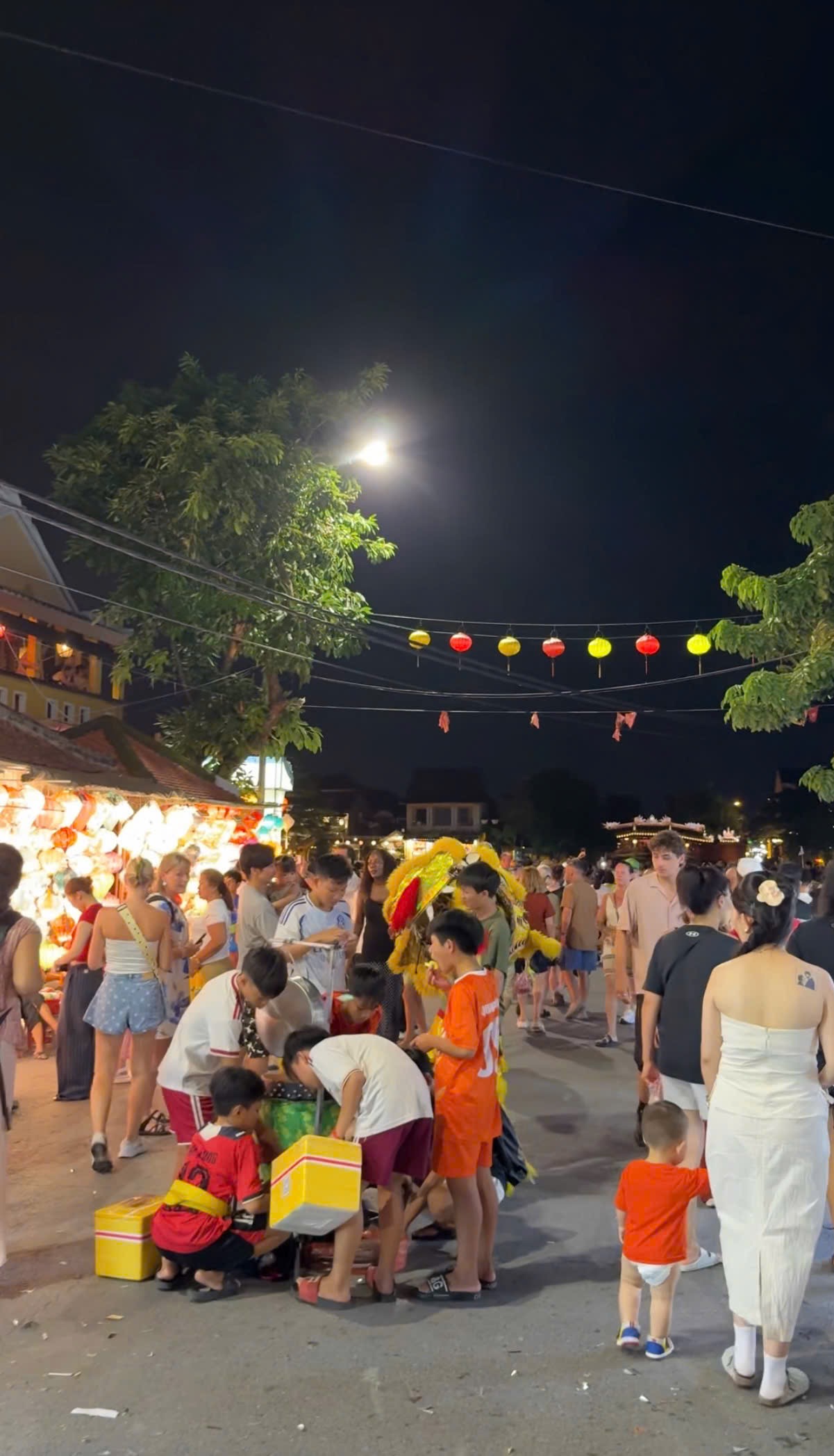The Mid-Autumn full moon shining over trees and strings of lanterns in Hoi An