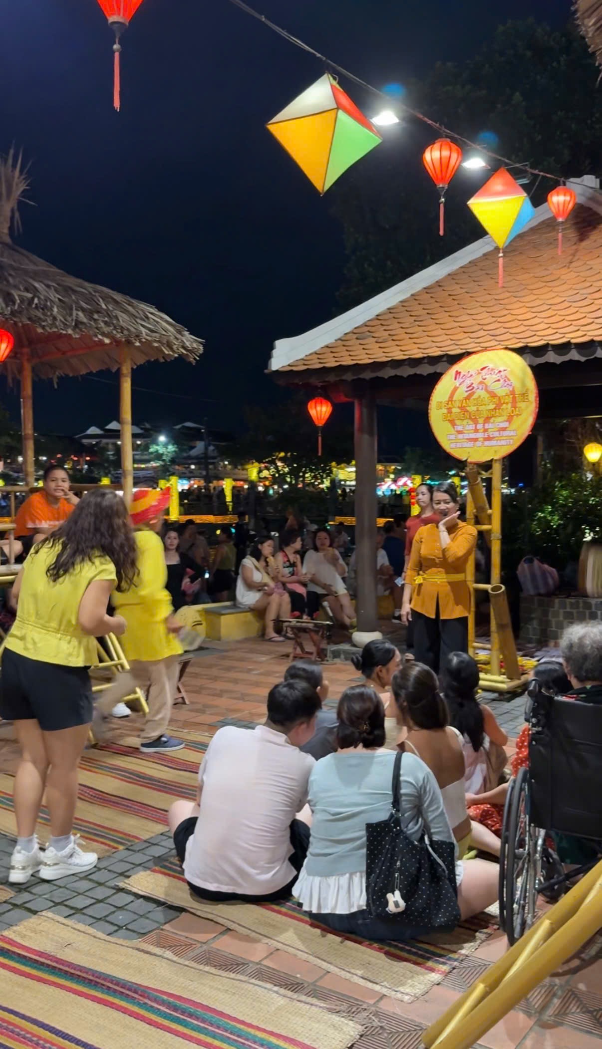 Colourful star and diamond-shaped Mid-Autumn lanterns hanging under a thatched roof in Hoi An at night