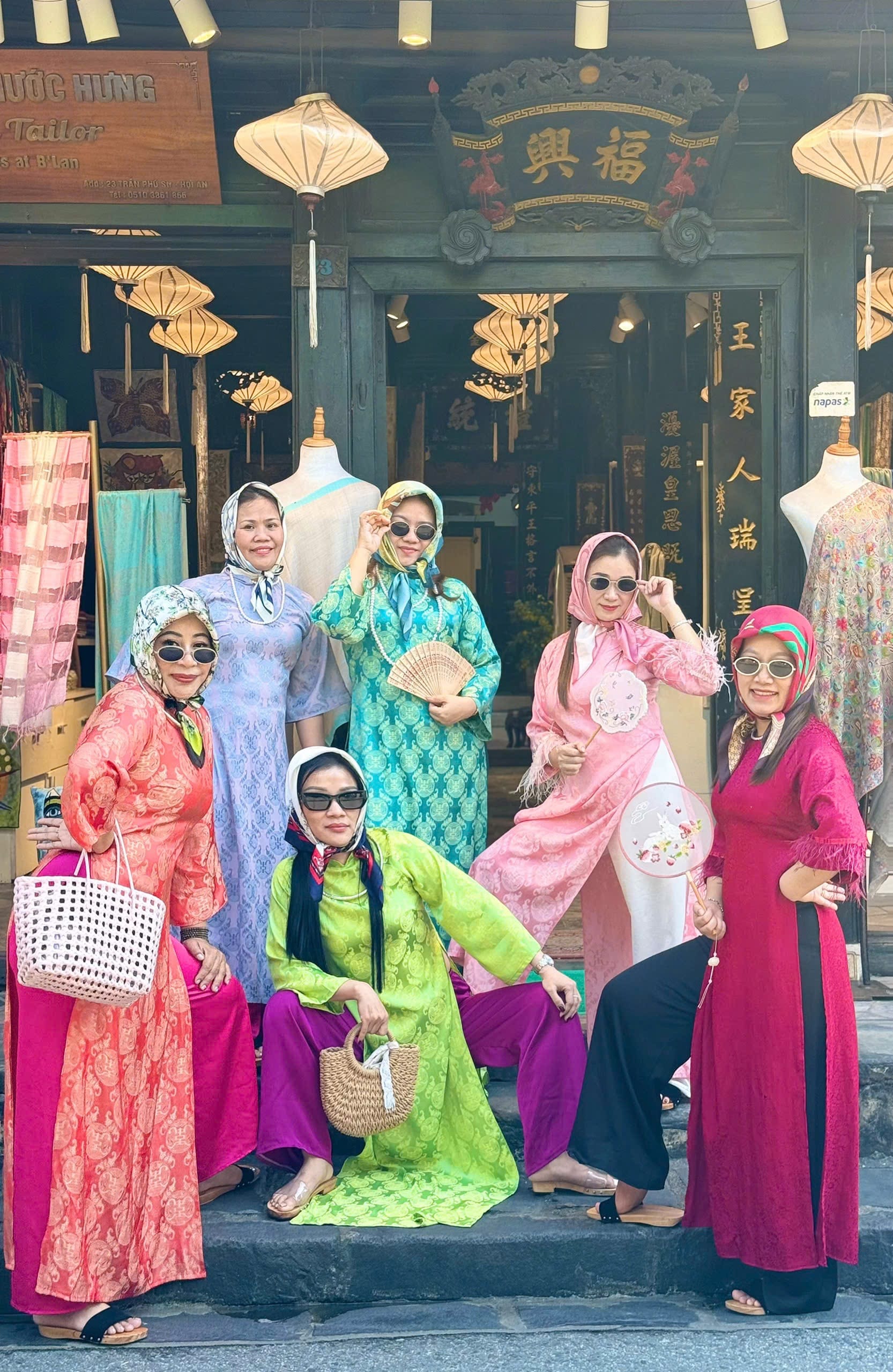A group of friends in colourful traditional Vietnamese dress posing at an old Hoi An shophouse hung with lanterns