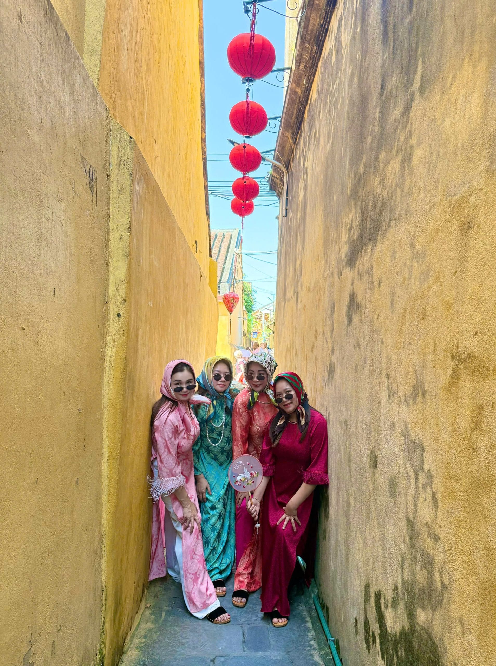 Friends in colourful traditional Vietnamese dress in a narrow yellow-walled Hoi An alley under red lanterns