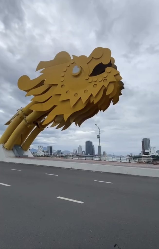 Dragon Bridge Da Nang during the day, dragon head against a cloudy sky with the city skyline in the background