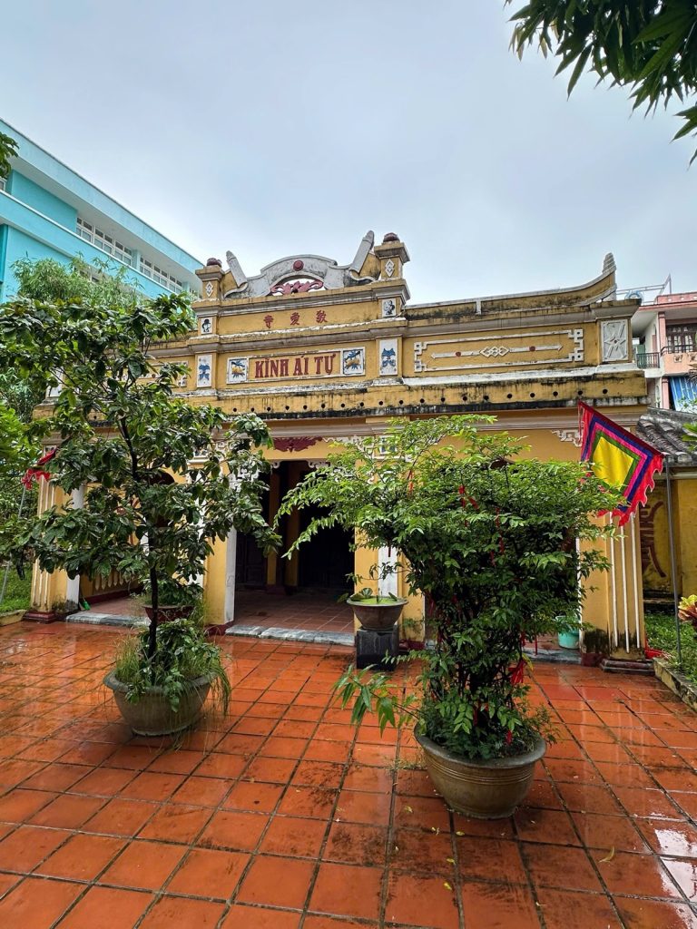 The yellow Kính Ái Tự shrine in the grounds of Hải Châu Village Temple, Da Nang, with potted trees and a festival flag