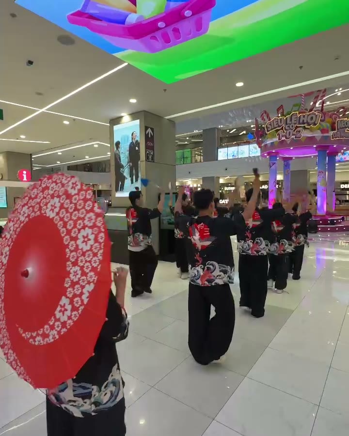 Yosakoi dancers in black and red costumes with red paper umbrellas parading through AEON Mall Da Nang