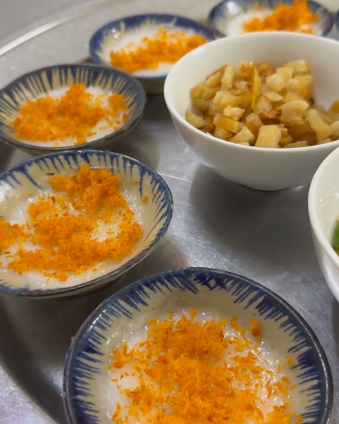 Tray of bánh bèo bọt biển topped with orange cá chấy, with bowls of tóp mỡ and chili fish sauce, at Thanh Hải in Da Nang