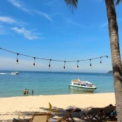 String lights hanging between palm trees over a white-sand beach and turquoise sea on Cù Lao Chàm, with a speedboat moored offshore
