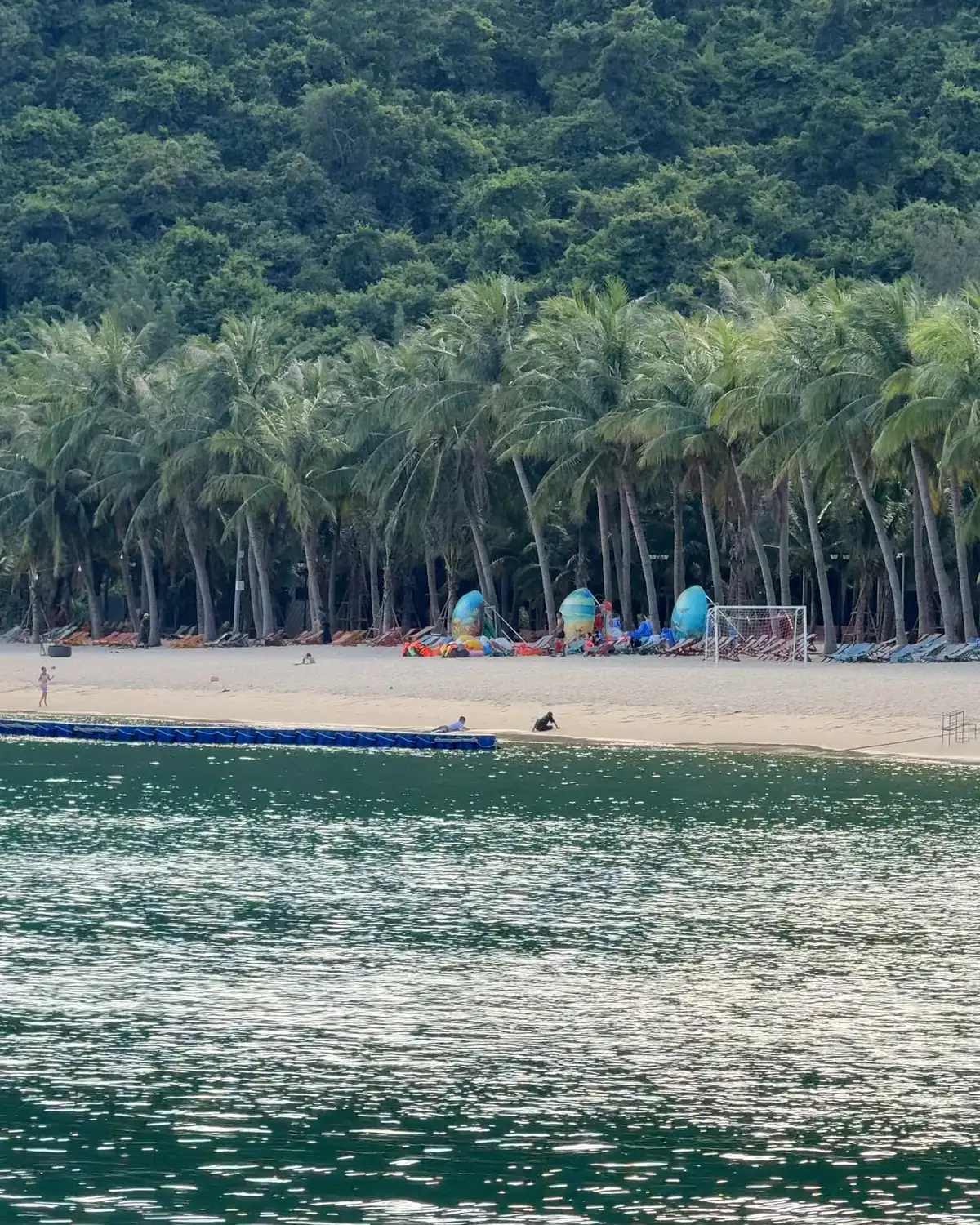 A long coconut palm beach at the foot of a forested hill on Cù Lao Chàm, seen from a boat on the green water