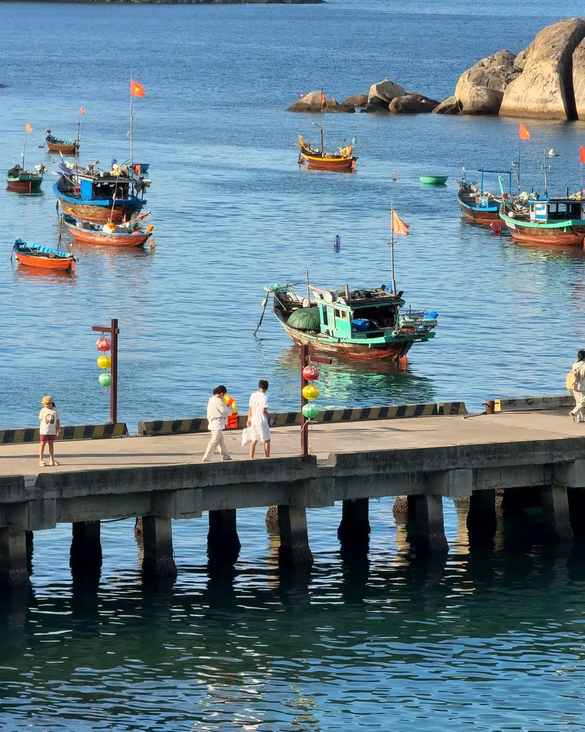 Colourful wooden fishing boats around the pier of the fishing village on Cù Lao Chàm, with a small green island behind