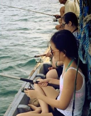 Friends fishing with rods from the side of a wooden boat off Cù Lao Chàm