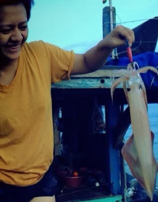 A local fisherman holding up a freshly caught squid on a wooden boat off Cù Lao Chàm