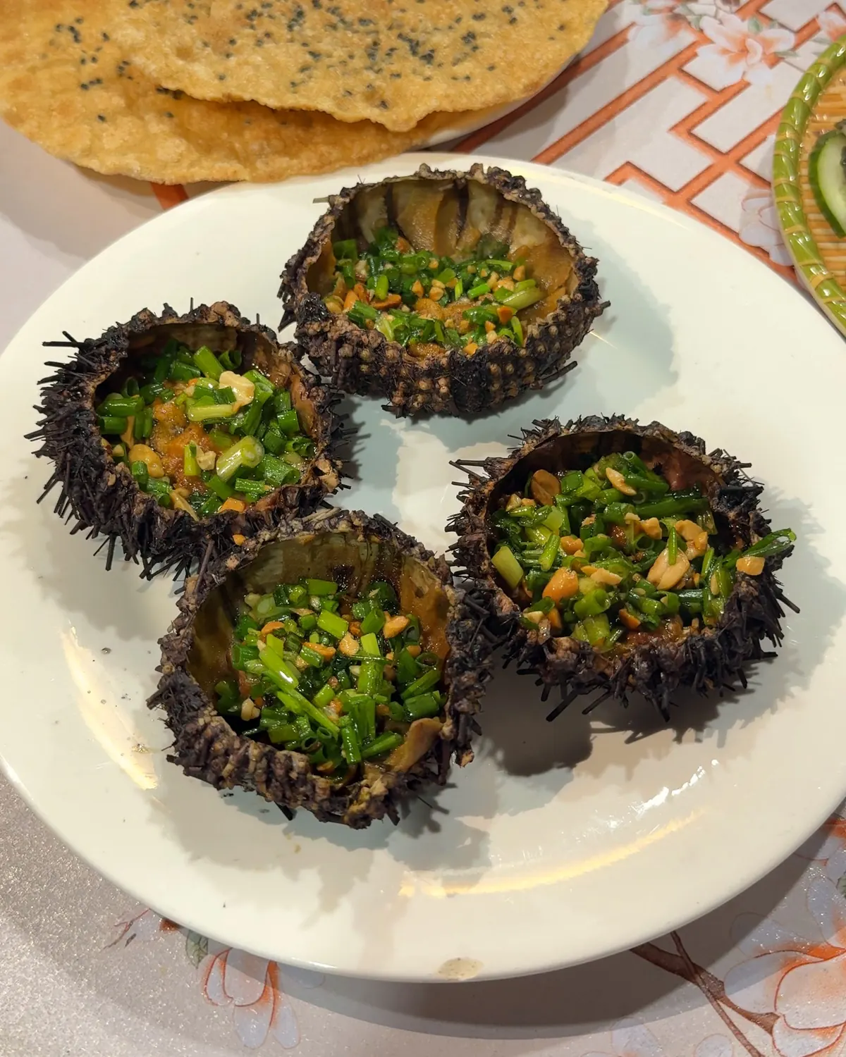 Grilled sea urchins topped with spring onion and peanuts, served with sesame rice crackers on Cù Lao Chàm