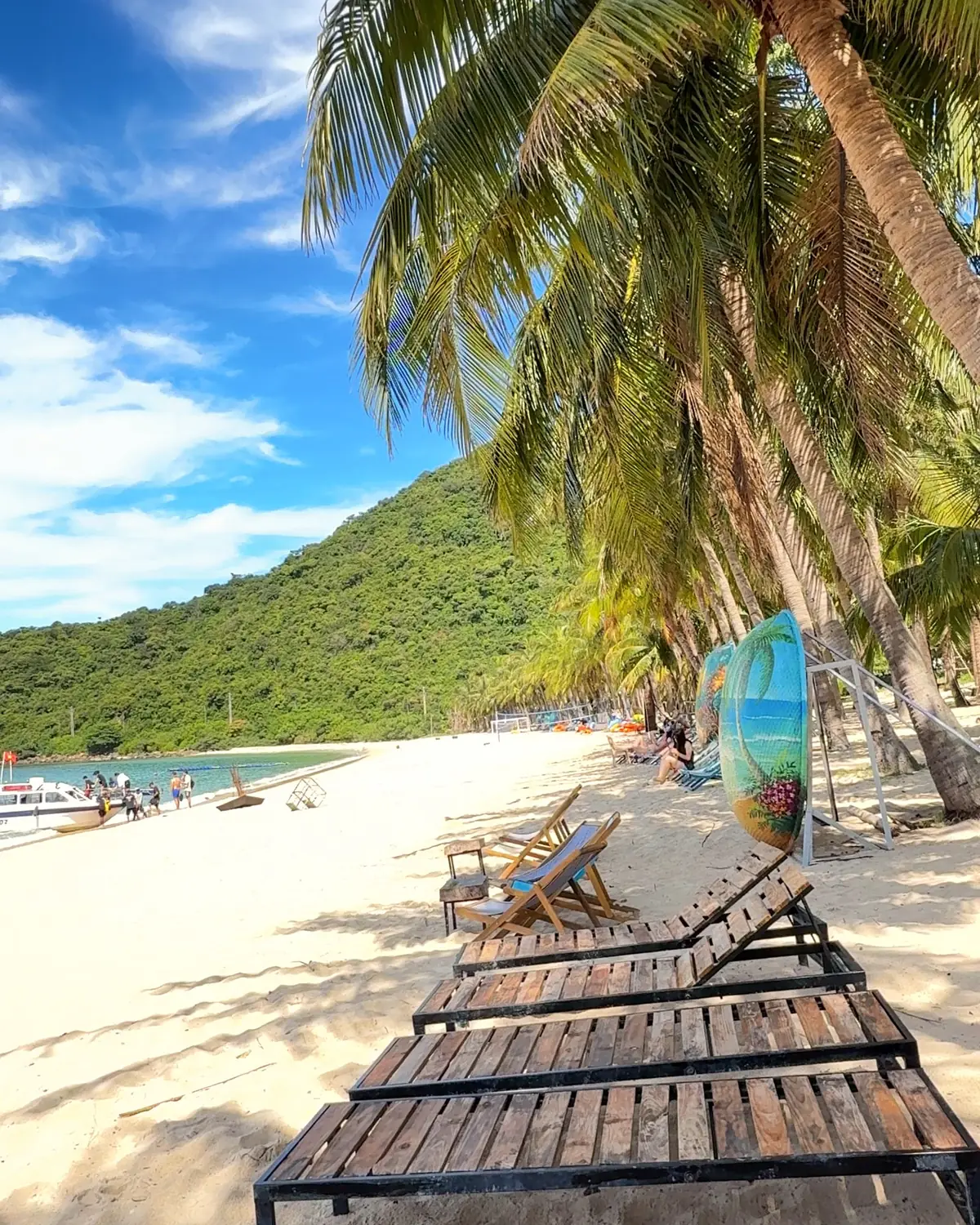 Wooden sunbeds under leaning coconut palms on a white-sand beach on Cù Lao Chàm