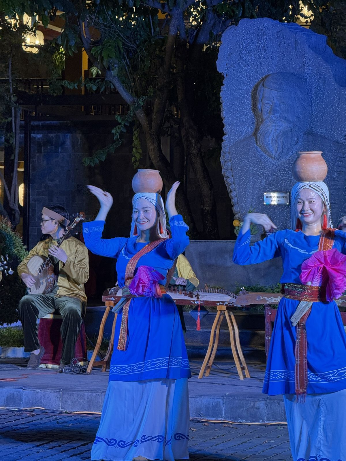 Dancers in blue costumes balancing clay pots on their heads during a Cham-style dance in Hoi An