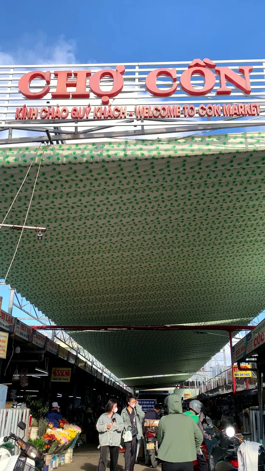 The entrance sign of Con Market reading "Welcome to Con Market" above a covered lane of stalls in Da Nang