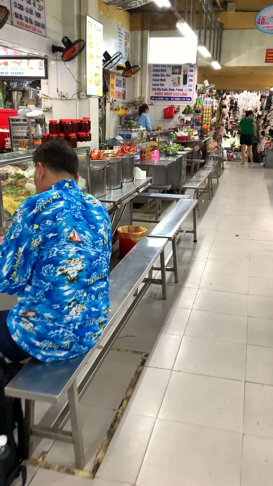 The long indoor food court at Con Market with stainless-steel tables, benches and food counters