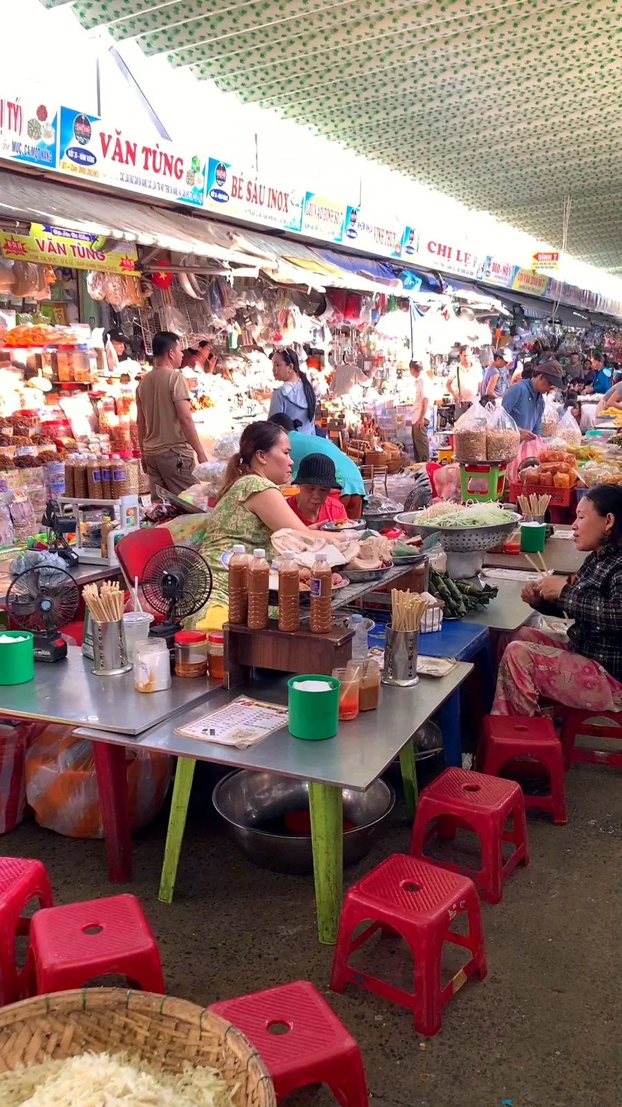 Low tables and red plastic stools at the snack area of Con Market, with a basket of shredded green papaya and chopstick holders