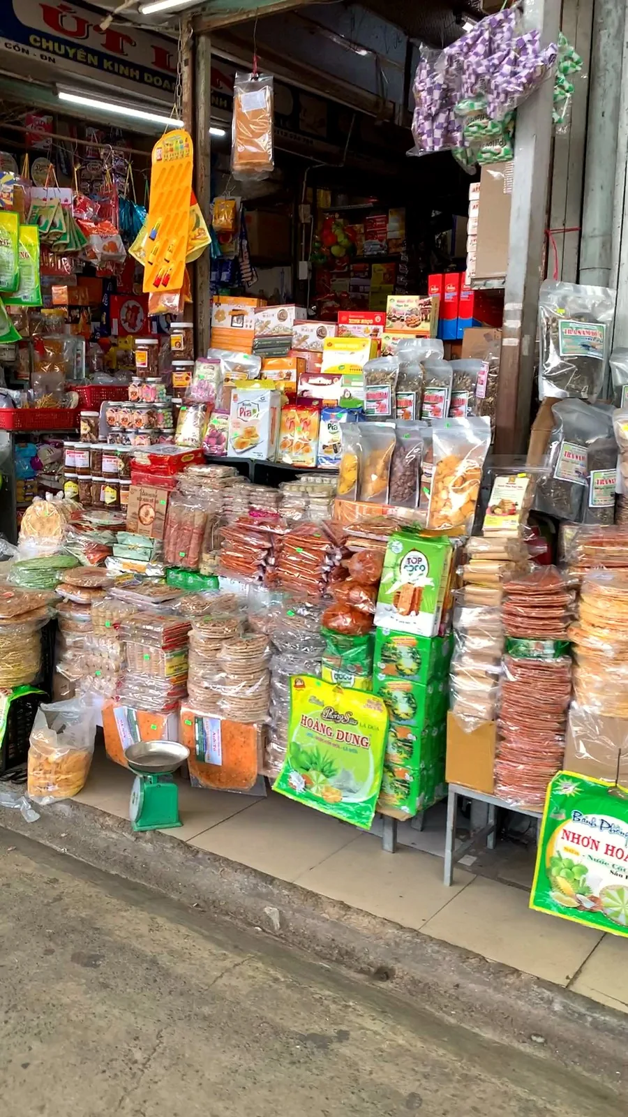 A packed snack stall at Con Market selling rice crackers, boxed pastries and bags of pandan-scented trà sâm dứa tea