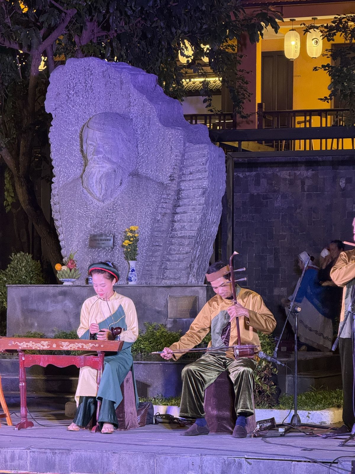 Musicians playing the dan tranh zither and dan nhi two-string fiddle in front of the Kazik statue in Hoi An