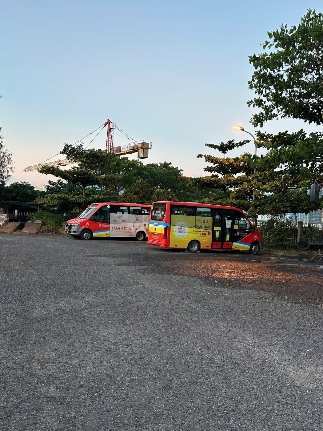 Two red and yellow FUTA minibuses parked at a bus station in Da Nang at dawn