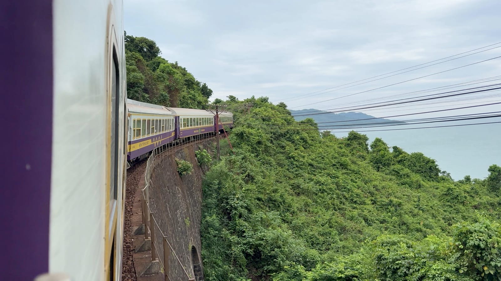 The purple and cream Hue – Da Nang Heritage Train on the cliffs above the sea at Hai Van Pass