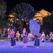 Folk arts program on stage at Kazik Park, Hoi An: a comic folk skit with an old man and two women in front of the Kazik memorial