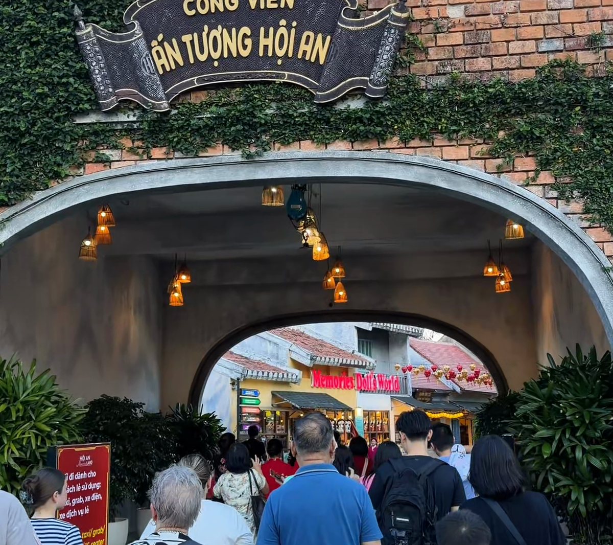 Visitors walking through the arched stone gate of Công Viên Ấn Tượng Hội An (Hoi An Impression Theme Park), covered in creepers and lanterns