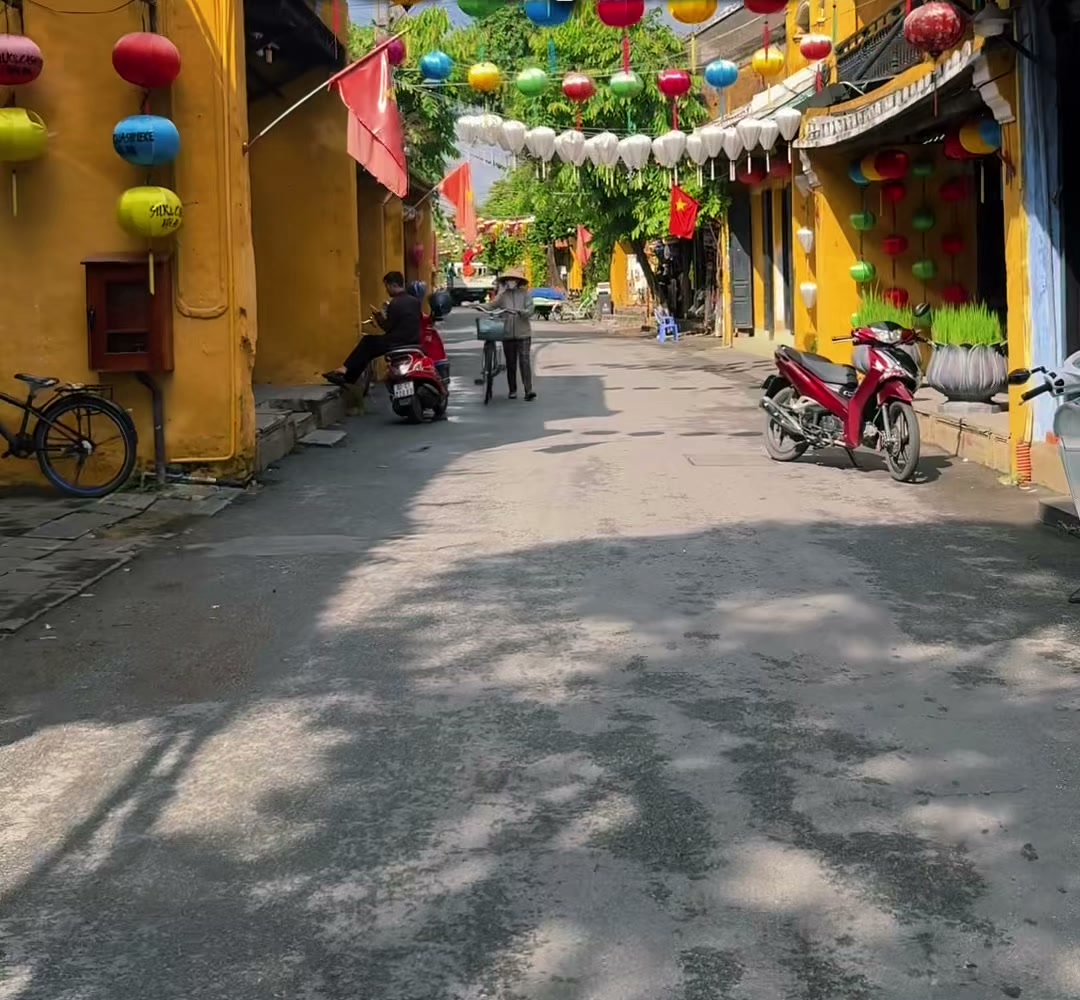 Colourful lanterns over a quiet yellow-walled street in Hoi An Old Town with only a few people, October 2026