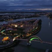Aerial view at dusk of Hoi An Memories Land lit up on its island in the Hoài River, with Hội An Old Town and the mountains behind