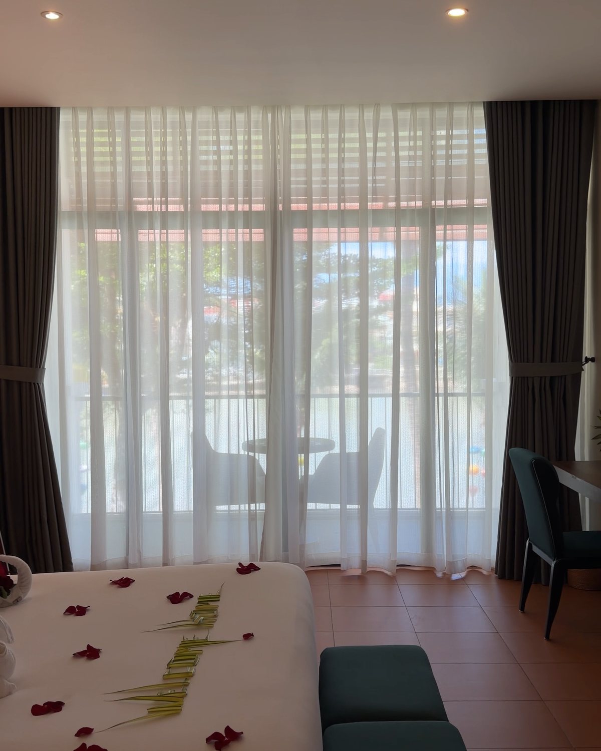 Sheer white curtains over tall windows in a Hoi An Memories Land room, looking out to a balcony and the town across the river