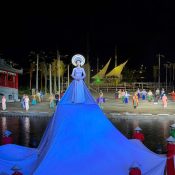 Hoi An Memories show finale: a woman in a white áo dài with a glowing halo headpiece stands on a huge blue-lit train on the river stage, with performers in áo dài and conical hats around her