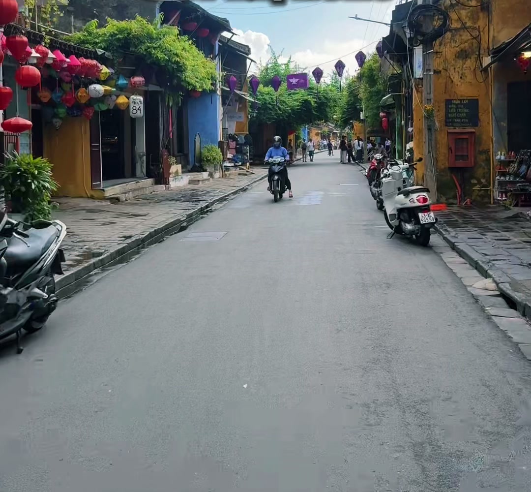 A long, almost empty street in Hoi An Old Town lined with yellow houses and lanterns under a blue sky, October 2026