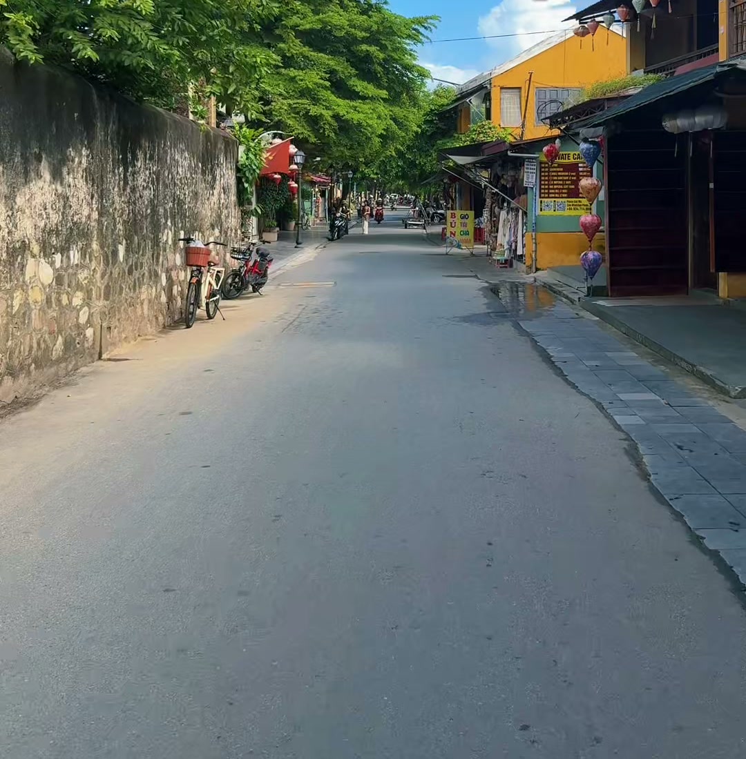 An empty lane beside an old stone wall and yellow houses in Hoi An Old Town under a blue sky, 20 October 2026
