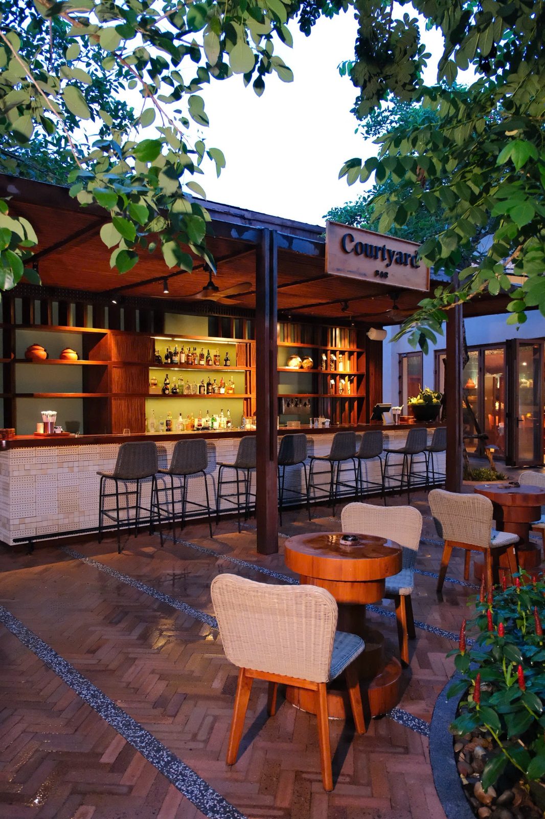 Open-air Courtyard Bar with wooden bar stools and rattan chairs under trees at Hoiana Resort & Golf
