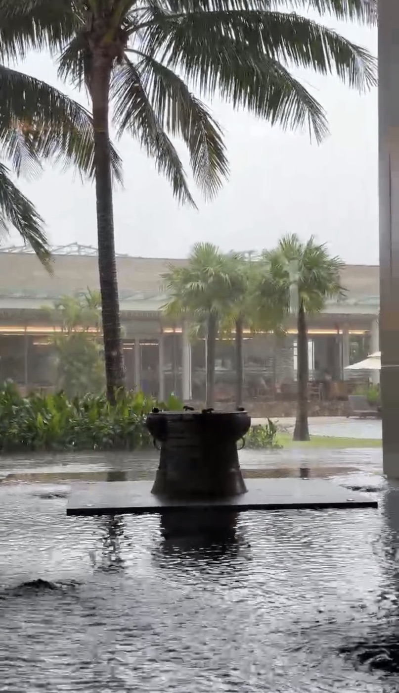 Heavy rain pouring over a bronze drum water feature and palm trees in the courtyard at Hoiana Resort & Golf