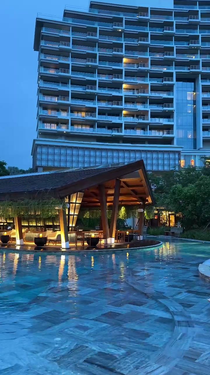 NOX Beach Club pool and lit pavilion with the New World Hoiana Hotel tower behind at dusk