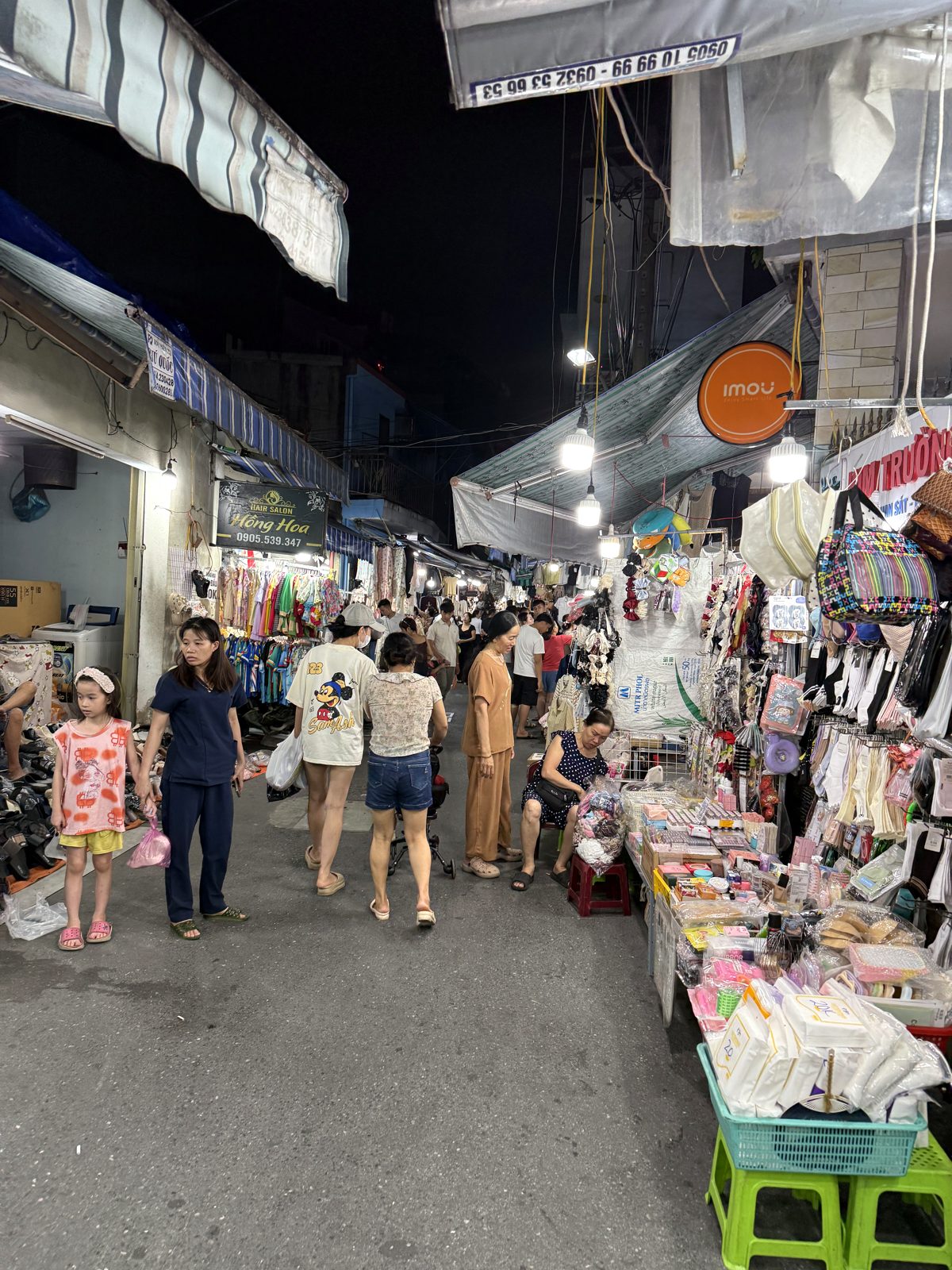 Crowds of young shoppers walking down the narrow lit-up alley of Le Duan Night Market in Da Nang at night