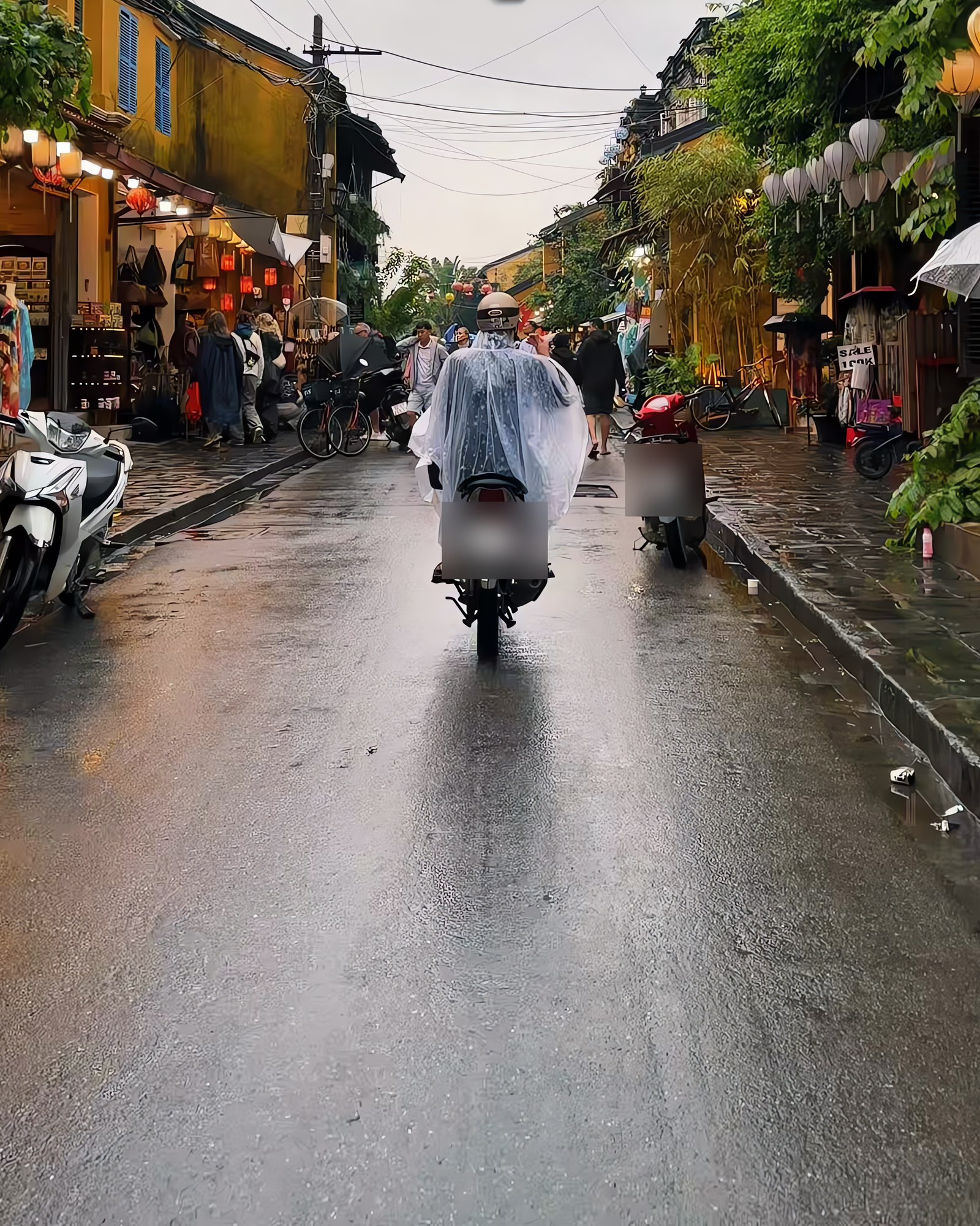Motorbike rider in a clear rain poncho on a wet street in Hoi An old town