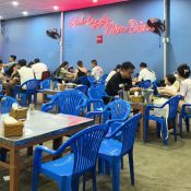Large dining hall with blue plastic chairs and the neon Năm Đảnh sign at the seafood restaurant in Da Nang