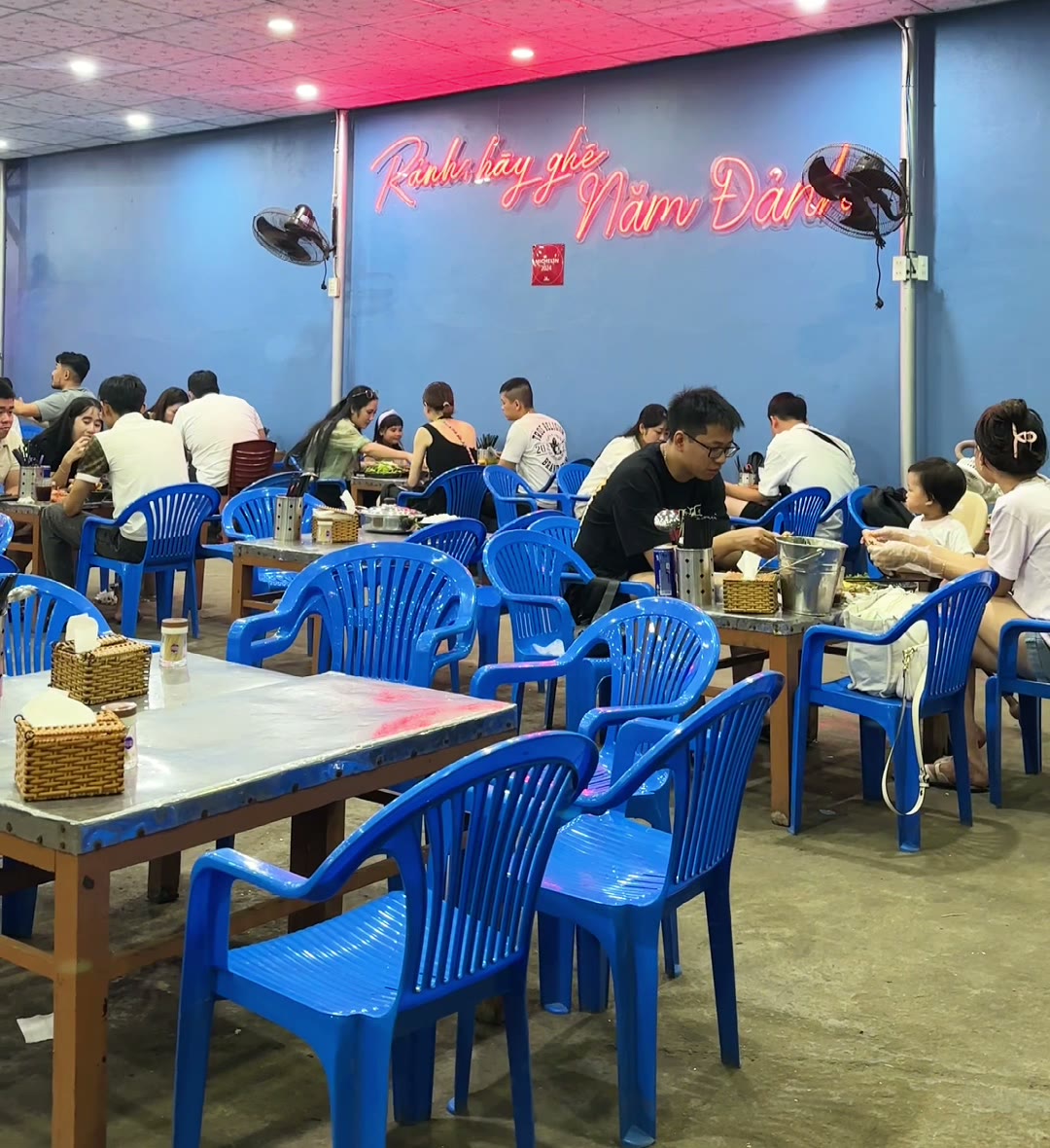 Large dining hall with blue plastic chairs and the neon Năm Đảnh sign at the seafood restaurant in Da Nang