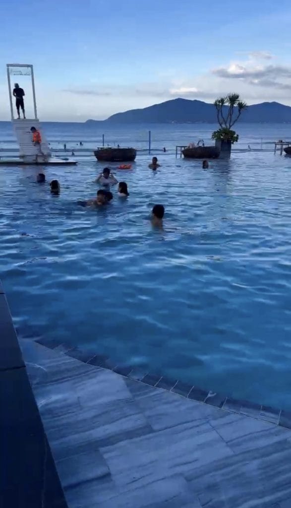 Swimmers in the infinity pool at Nami Beach Club with Da Nang Bay and the mountains behind