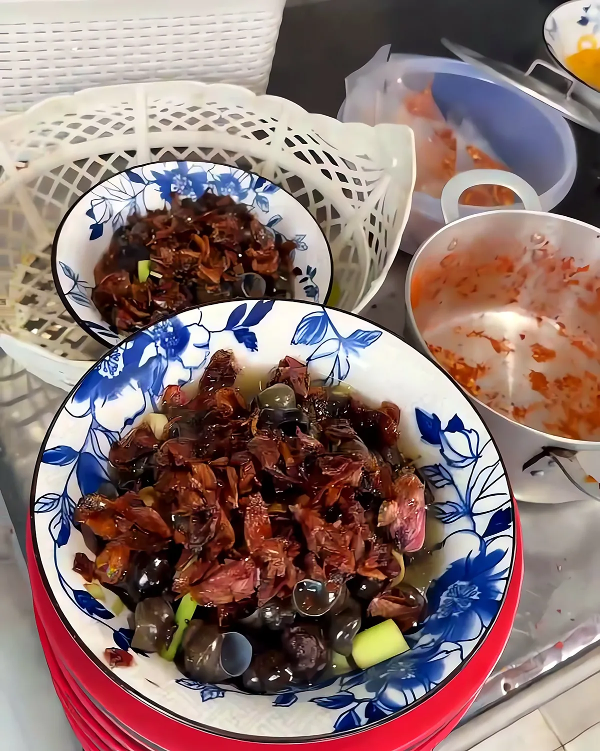 A finished bowl of ốc hút topped with fried shallots, resting on a stack of red plates at a busy Da Nang stall