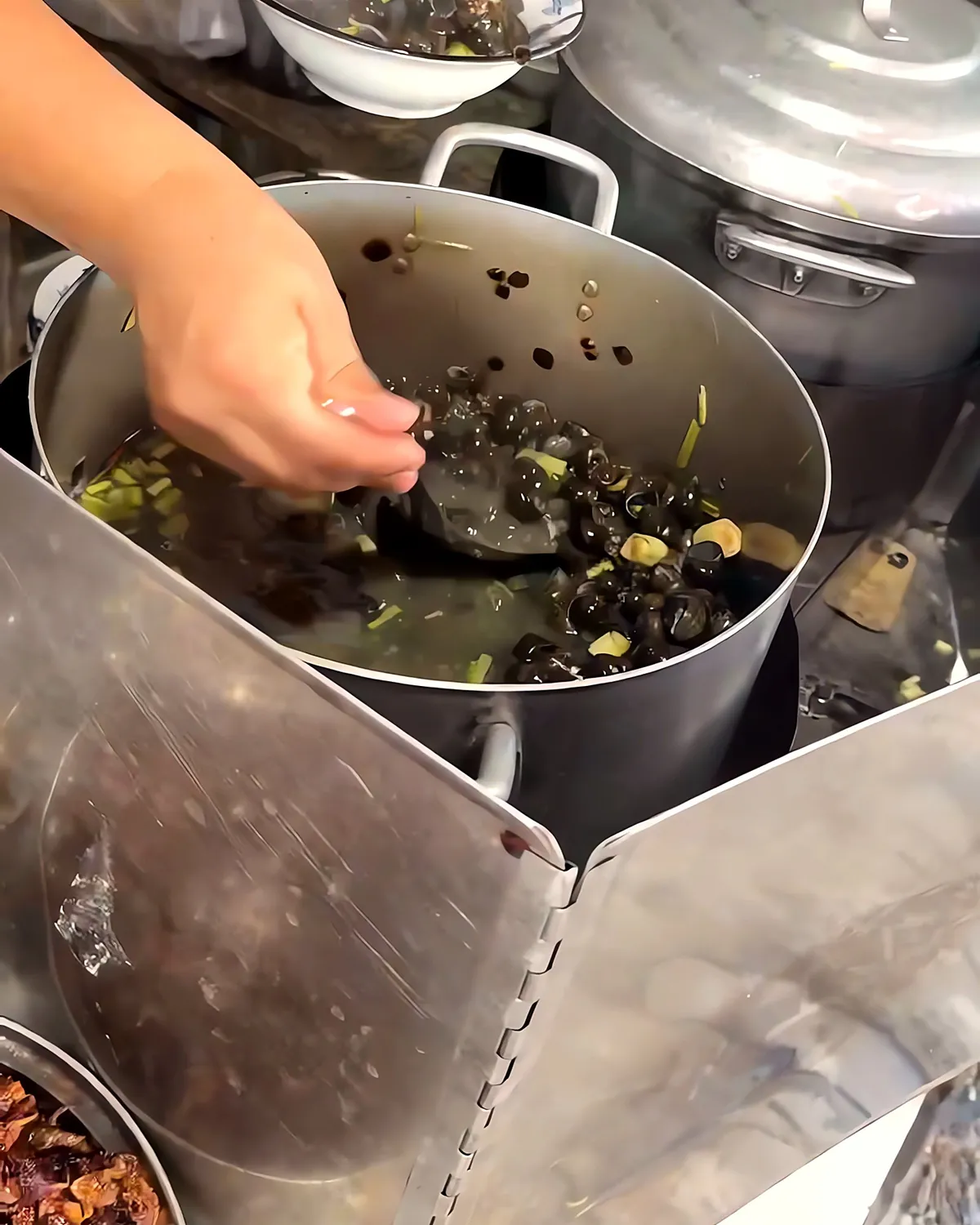 A vendor ladles small snails out of a big pot of lemongrass broth at Ốc hút Hạnh Điện Phương in Da Nang