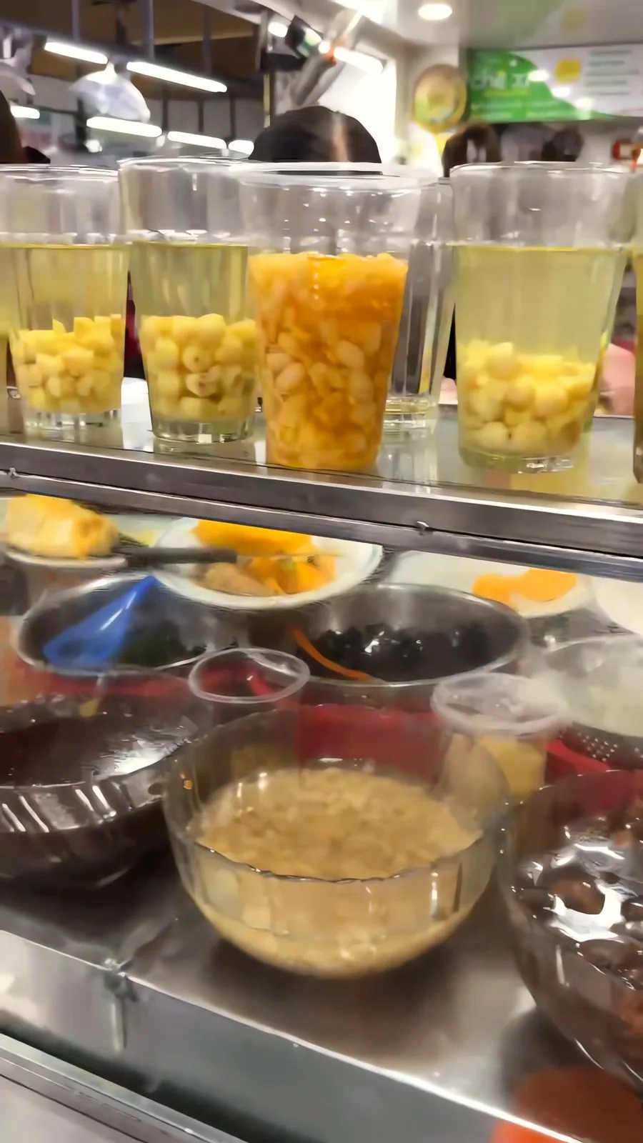 Glasses of chè lined up on the counter at Quán Hoa Xù in Con Market, with bowls of toppings below
