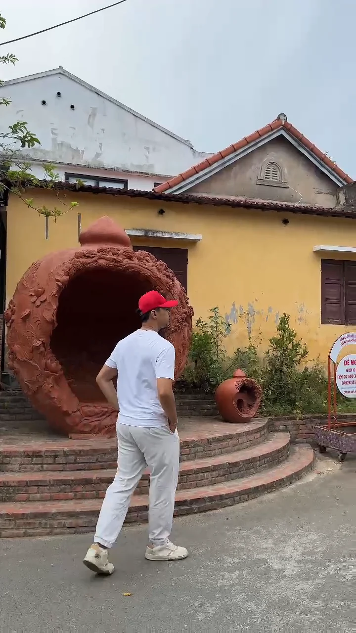 Giant terracotta jar sculpture beside a yellow house in Thanh Ha Pottery Village, Hoi An, with the Visit Da Nang presenter